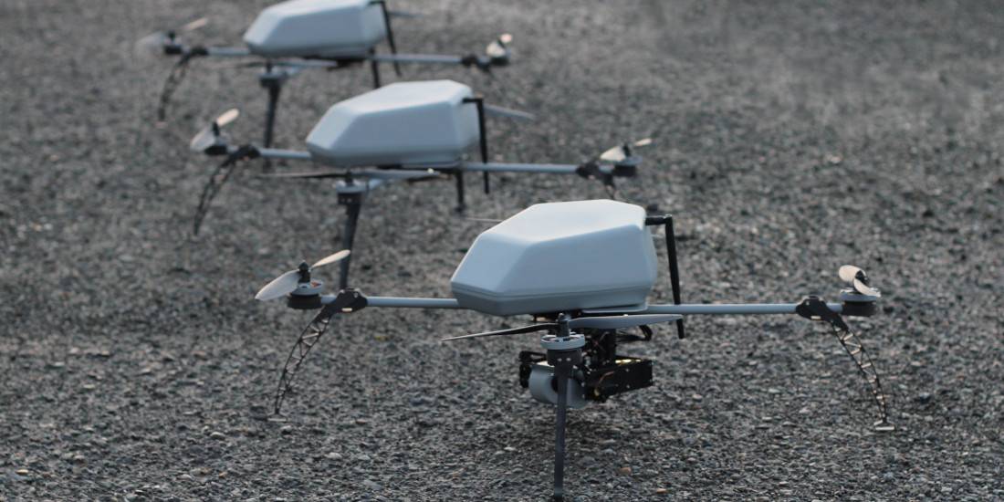 Three quadrotor drones resting on gravel