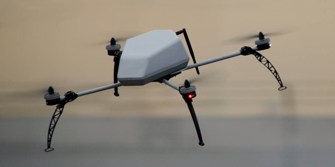 Quadrotor drone with a grey shell, in flight